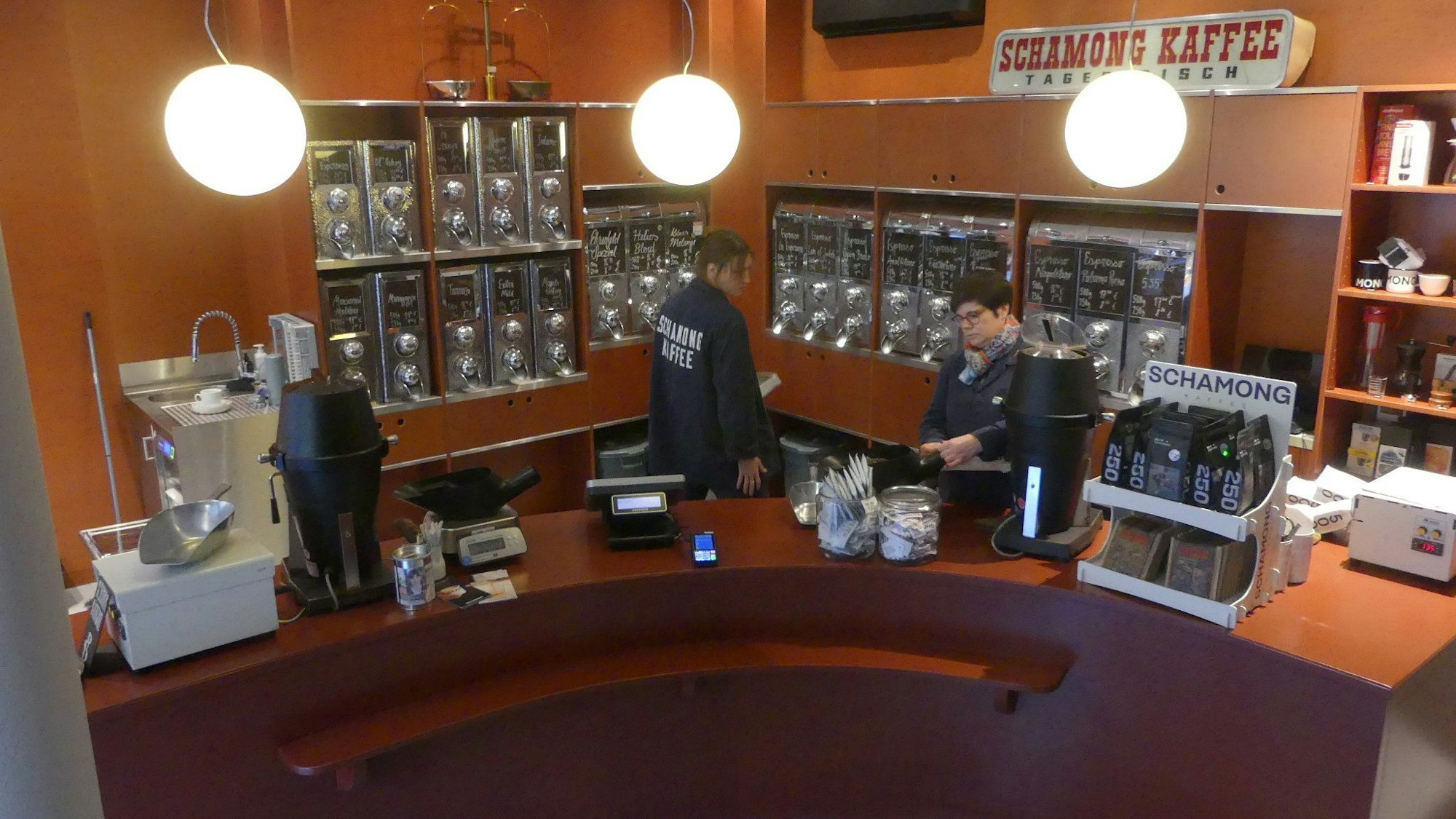Blick in den Verkaufsraum einer Kaffee-Rösterei mit halbrundem Verkaufstresen und vielen Kaffeebohnen-Behältern an der Wand