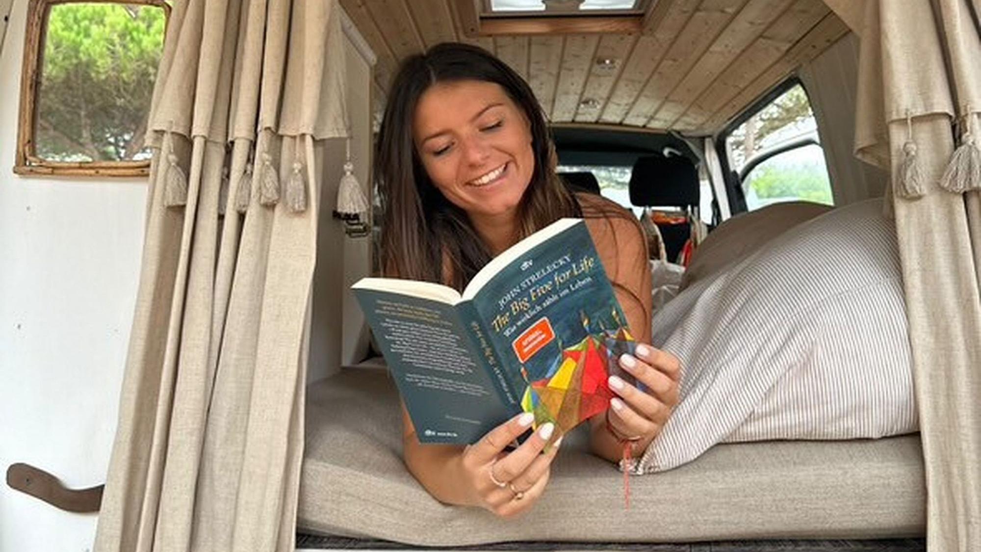 Anna Lüling liegt auf einer Matratze in einem Wohnwagen und hat das Buch „The Big Five for Life“ des Autors John Strelecky aufgeschlagen.