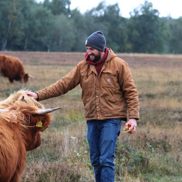 Gemeinsam mit mehreren schottischen Hochlandrindern steht Kilian Busch auf einer Weide in der Drover Heide und streichelt eine Kuh am Kopf