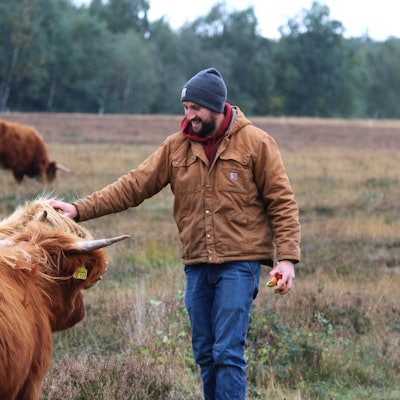 Gemeinsam mit mehreren schottischen Hochlandrindern steht Kilian Busch auf einer Weide in der Drover Heide und streichelt eine Kuh am Kopf