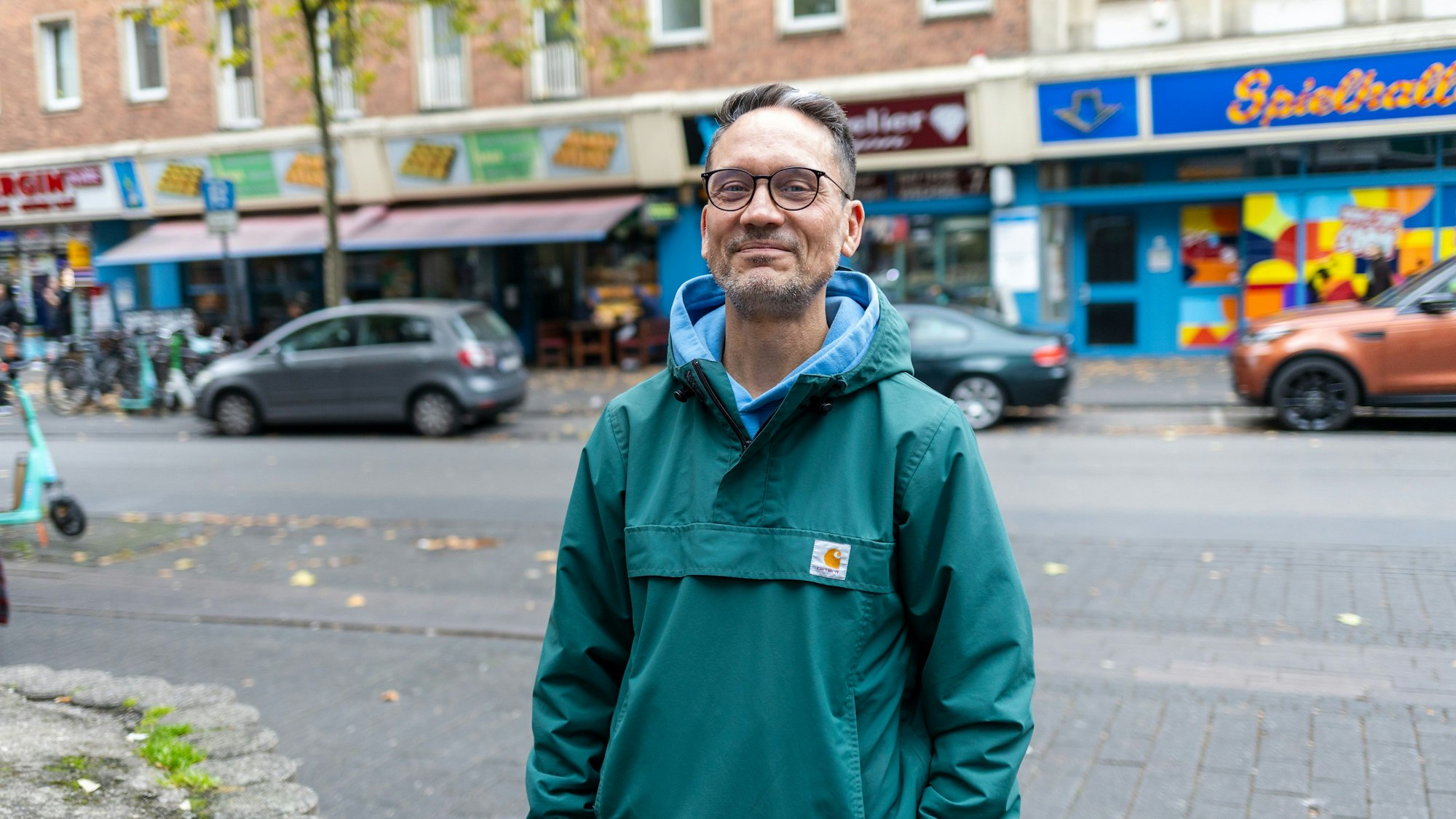 Ein Mann in einer grünen Jacke. Im Hintergrund ist die Venloer Straße zu sehen.
