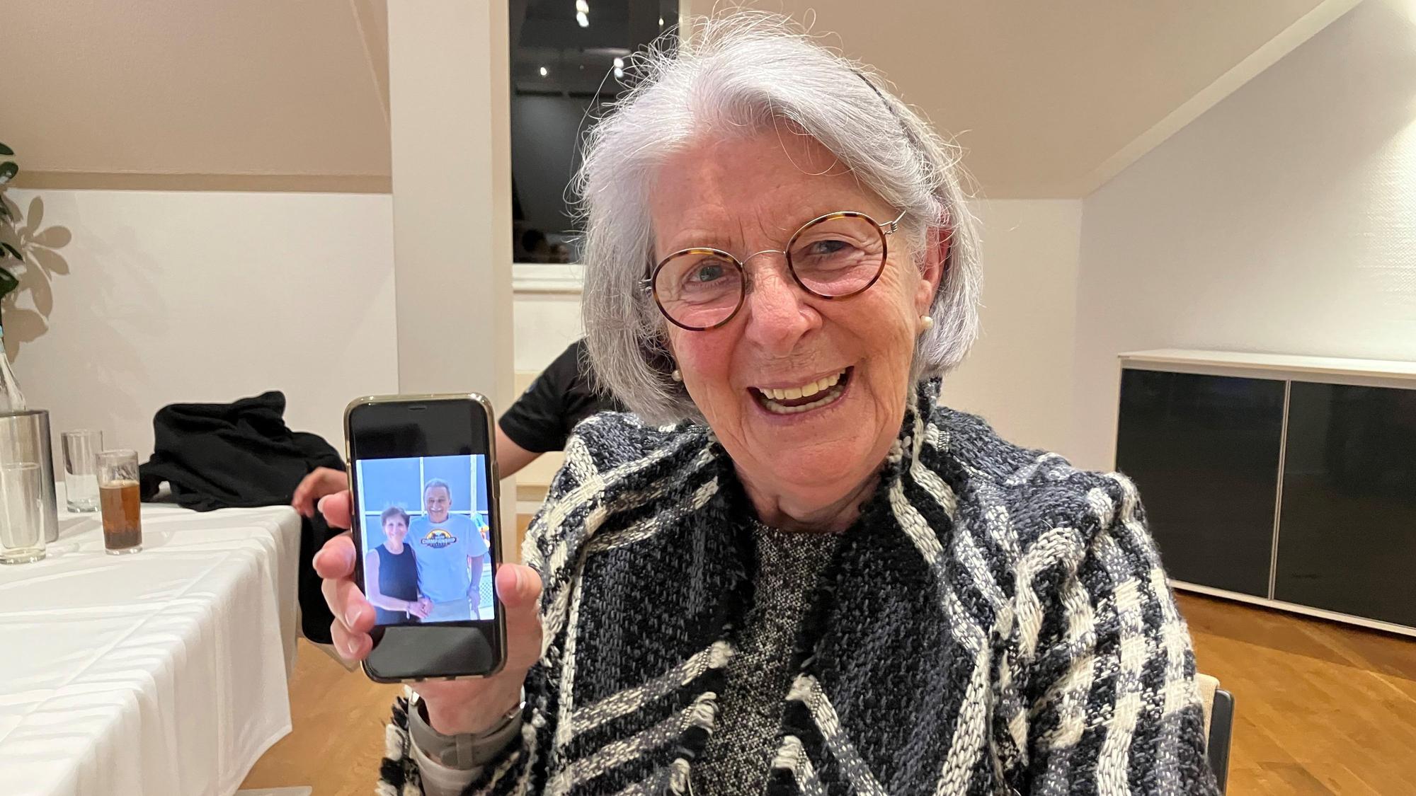 Eine ältere Dame zeigt ein Foto mit zwei Personen auf ihrem Handy.