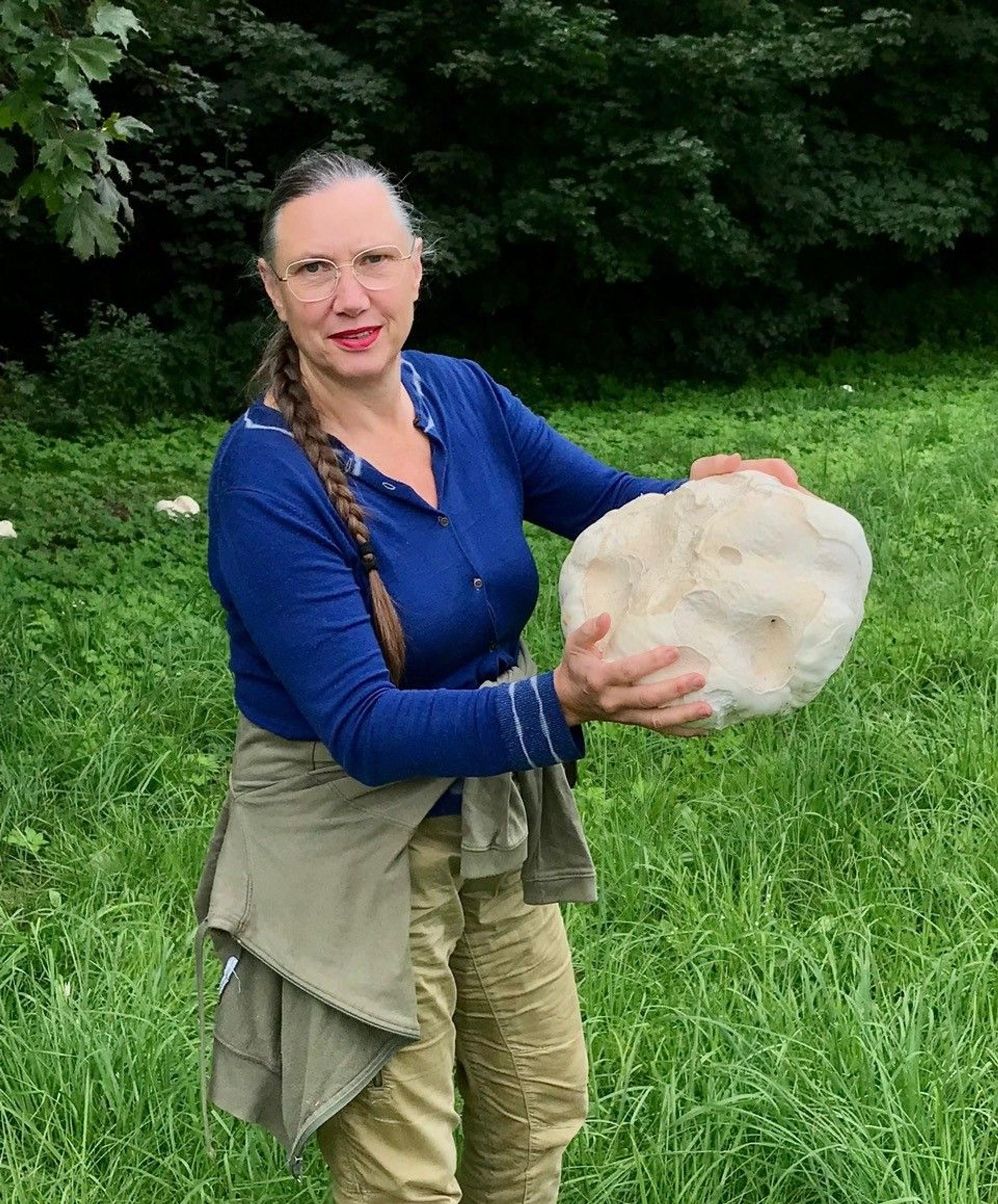 Eine Frau mit Zopf und Brille hält einen großen Stein in der Hand.