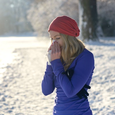 Eine erkältete Frau putzt sich auf einem Spaziergang durch den Schnee im Winter die Nase.