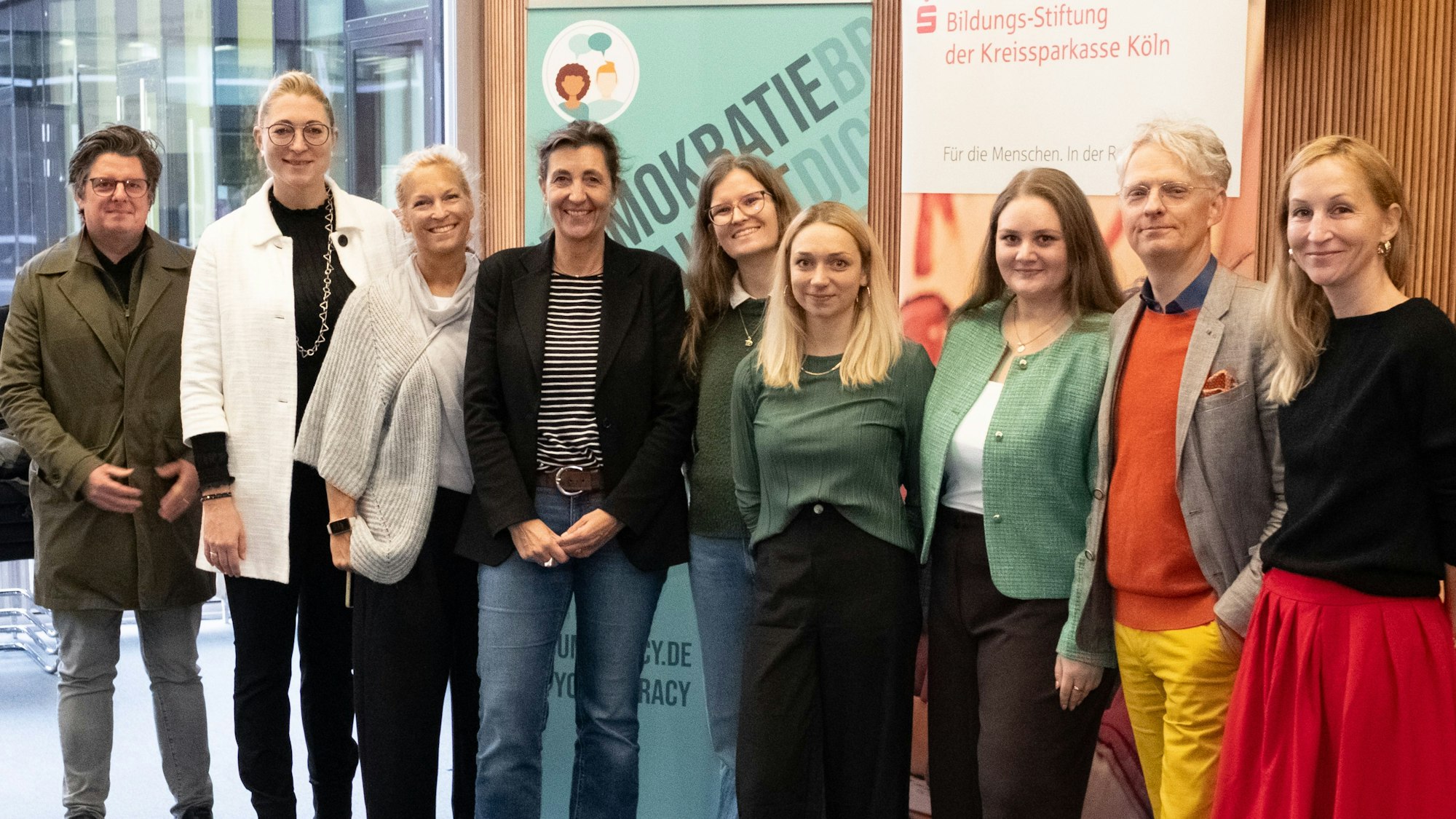 Junge Frauen und zwei Männer stehen in einem Sitzungssaal.