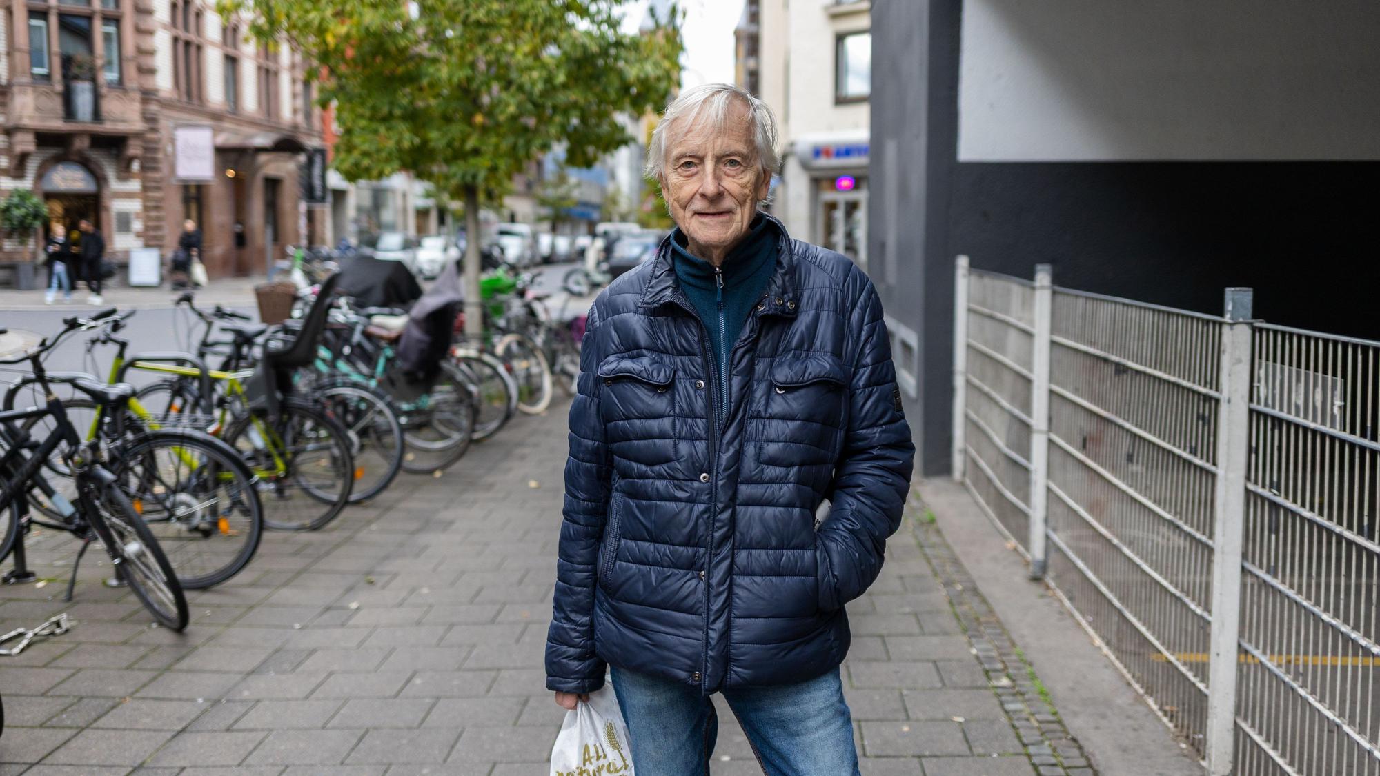 Ein älterer Mann mit Brötchentüten in der Hand steht auf der Maastrichter Straße.