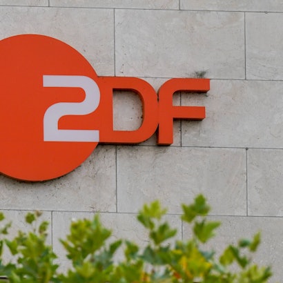 Orangefarbenes ZDF Logo an einer Steinwand, mit unscharfem Grün im Vordergrund