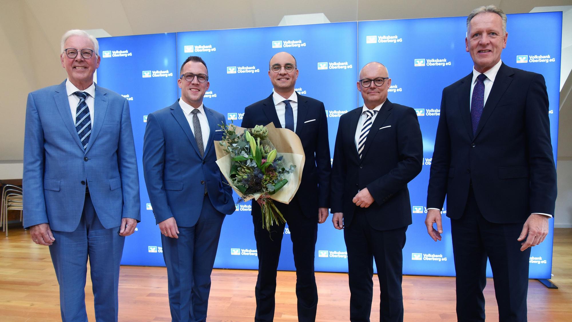 Fünf Herren im Anzug, der Mann in der Mitte hält einen Blumenstrauß.