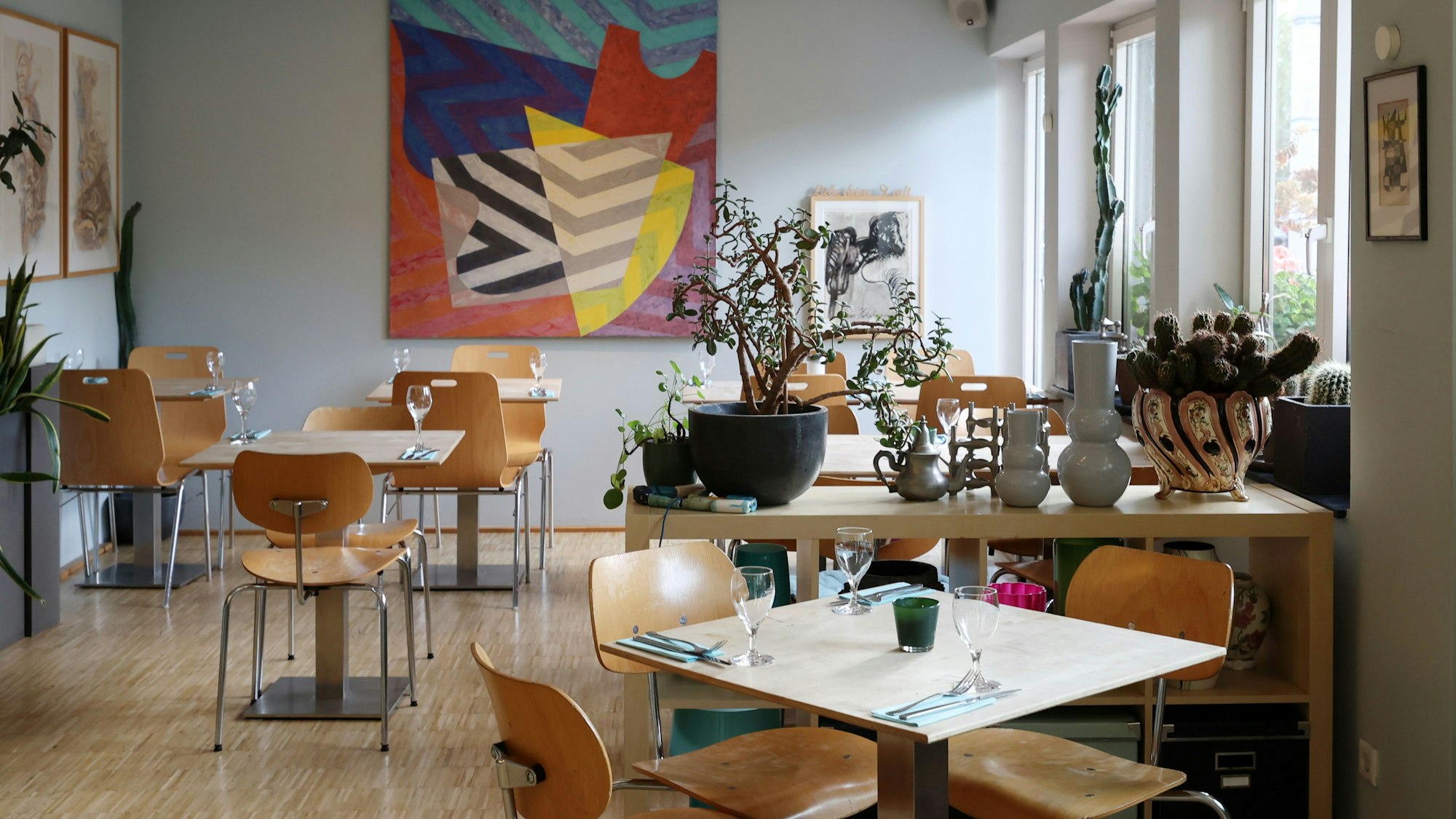 Innenraum des „Riphahn“: Holzstühle und Tische, eingedeckt mit Weingläsern, dekoriert mit Vasen, an der Wand hängt ein buntes Bild