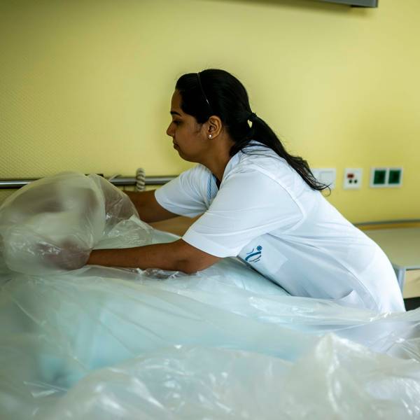 Zwei Pflegefachkräfte des Euskirchener Marienhospitals bringen eine Plastikfolie an einem frisch bezogenen Bett an.