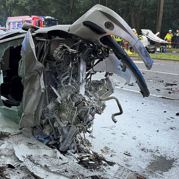 Ein Autowrack liegt ausgebrannt auf einer Straße.