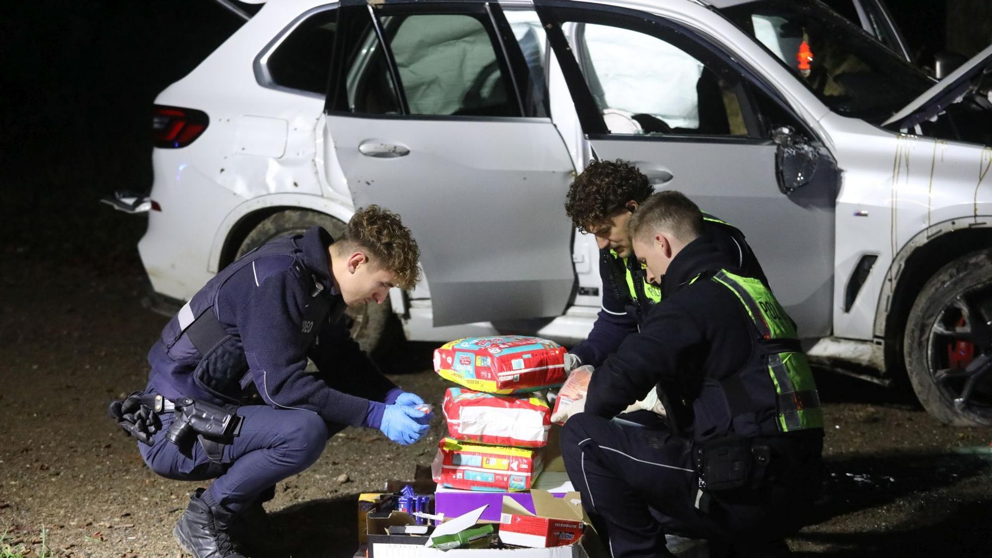 Drei Polizisten hocken auf dem Boden und sichten das gefundene Material aus dem BMW.