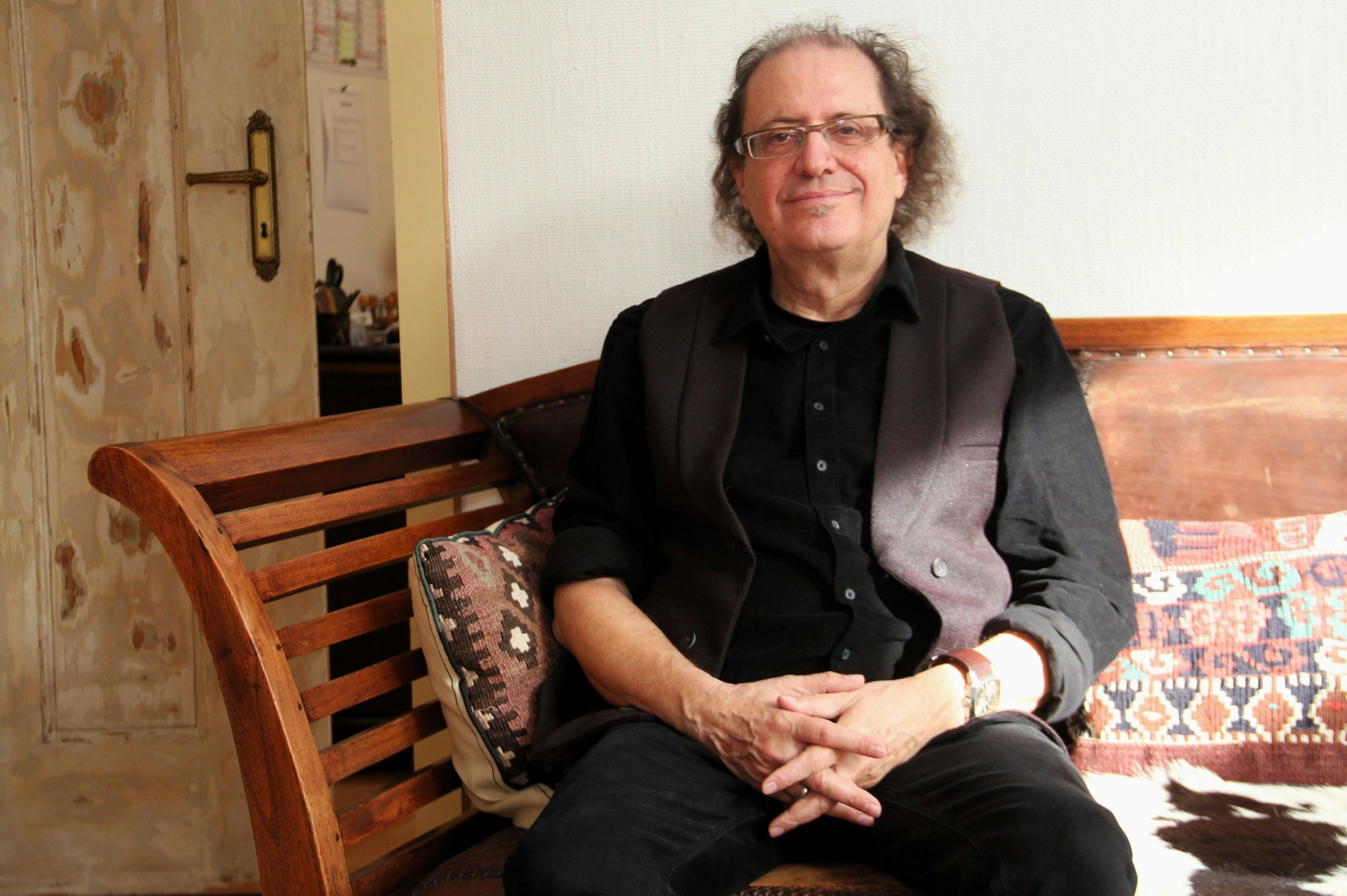 Ein Mann mit Brille im dunklen Anzug sitzt auf einem Sofa.