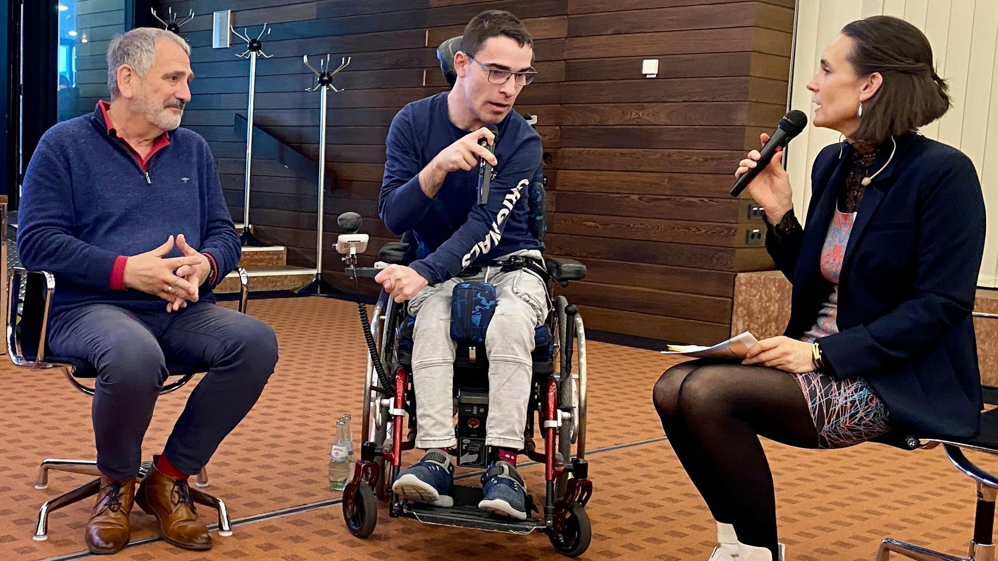 Silke Toennes interviewt Johannes Becker, der im Rollstuhl sitzt, und seinen Vater Frank.