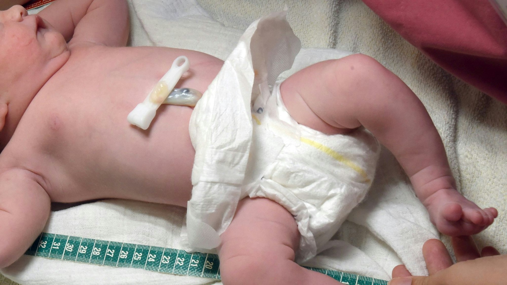 Ein Baby liegt in einer Windel auf einem Tuch, daneben ein Massband. (Symbolbild).