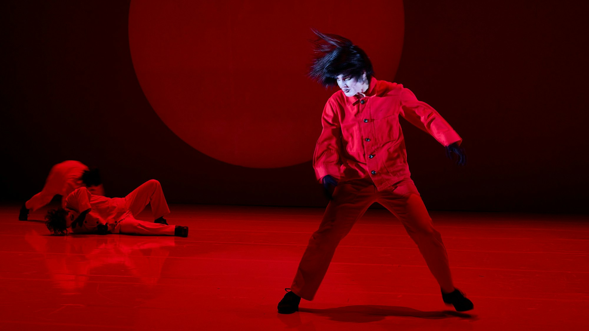 Die Bühne im Depot 1 ist in rotes Licht getaucht. Julia Schubert trägt einen roten Anzug und eine schwarze Perücke. Ihr Gesicht ist weiß geschminkt.