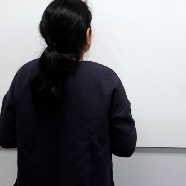 Ein Mädchen mit schwarzem Pferdeschwanz steht vor einer Tafel, auf der das Wort Rächschreibfela steht.