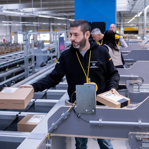 Mehrere Mitarbeiter sortieren kleine Pakete in den Multiformatsorter ein.