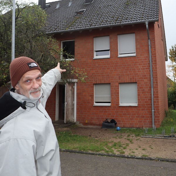 Zu sehen ist, wie ein Mann auf ein Haus deutet.