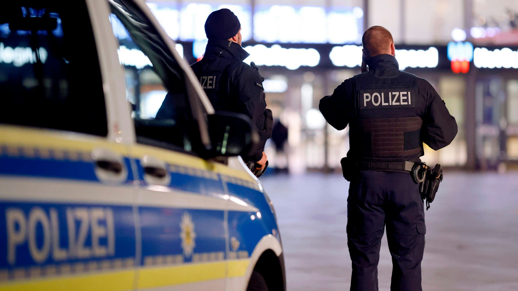 Zwei Polizisten stehen vor einem Polizeiwagen vor dem Hauptbahnhof in Köln.