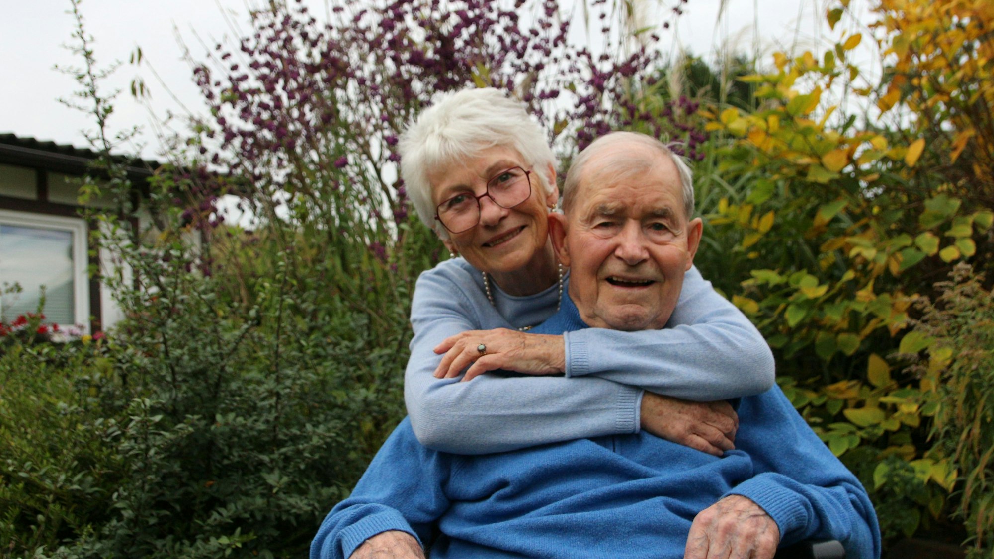 Eine Frau umarmt ihren Mann, sie wirken vergnügt und lächlen in die Kamera.