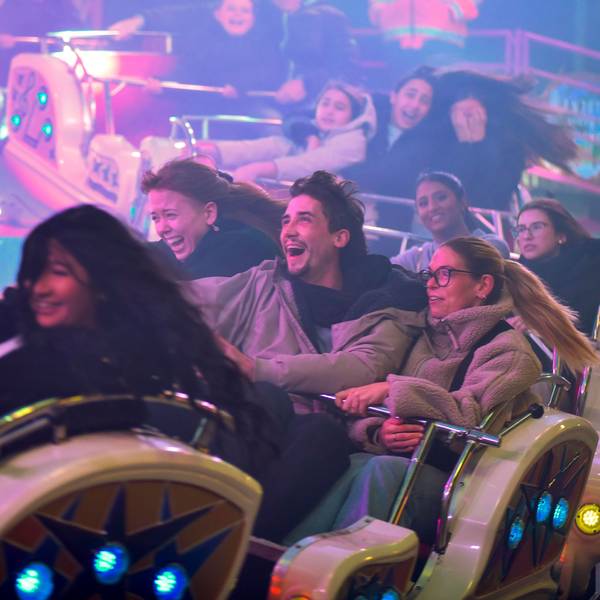 Zu sehen sind mehrere Menschen in einem Fahrgeschäft auf einem Rummelplatz.