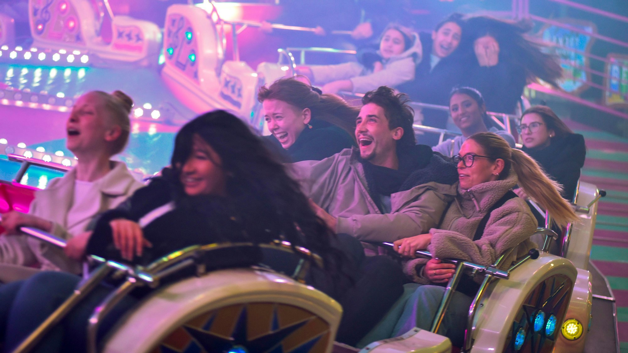 Zu sehen sind mehrere Menschen in einem Fahrgeschäft auf einem Rummelplatz.