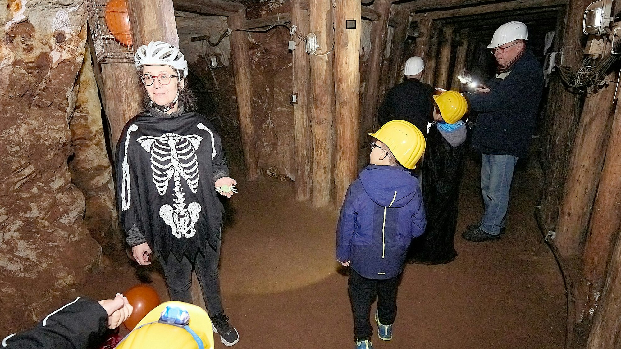 Petra Trimborn steht mit Besuchern in einem Bergwerksstollen. Sie trägt einen Knochen-Overall.