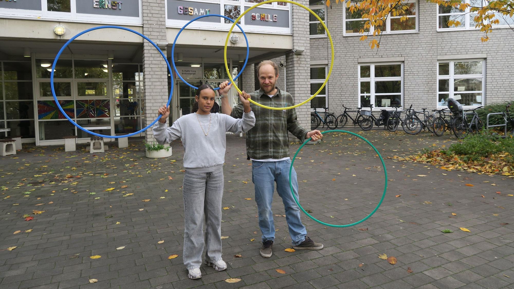 Ein Mädchen steht neben einem Mann im karierten Hemd. Sie halten unterschiedlich große Ringe in die Luft.