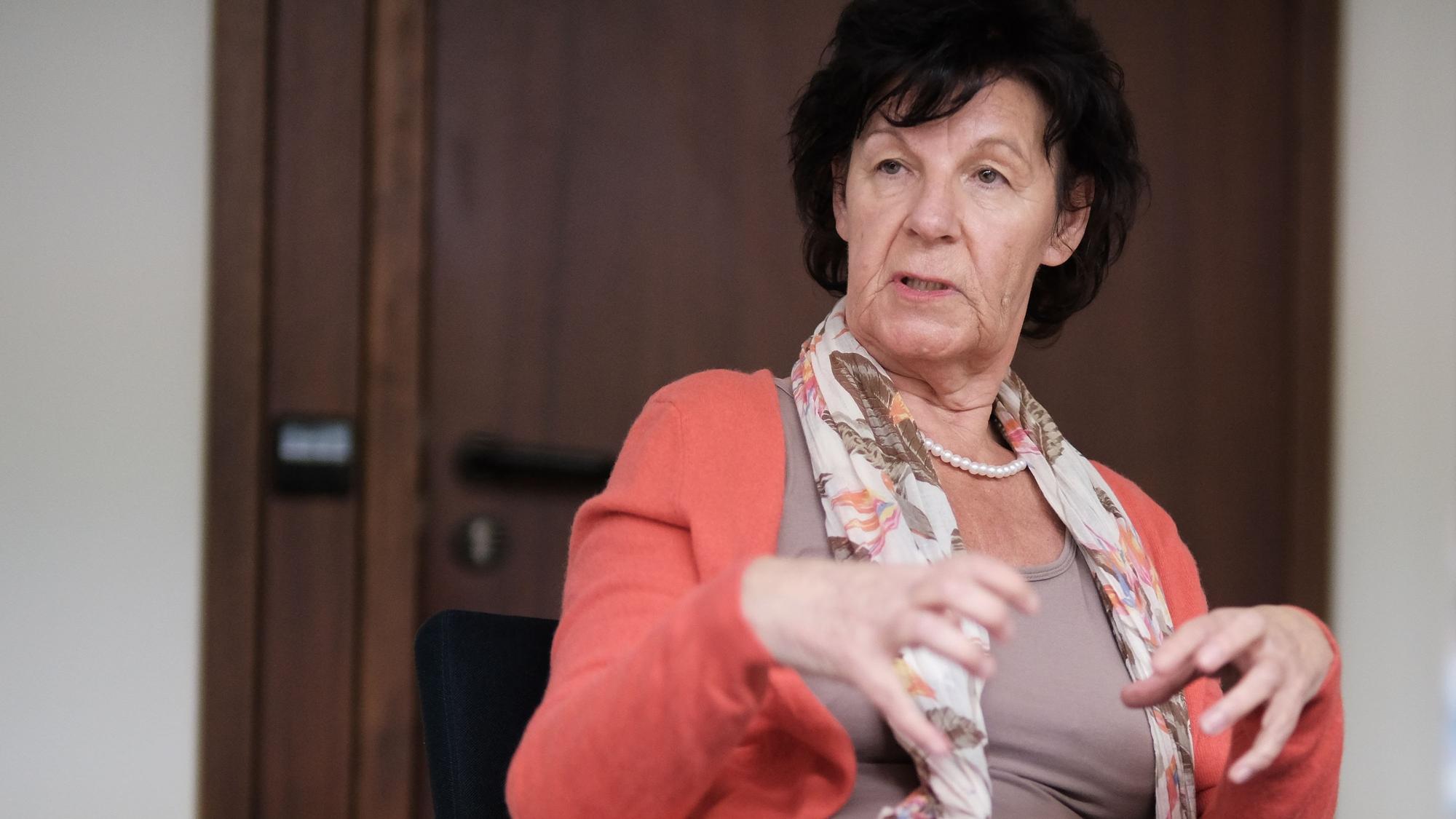 Eine Frau mit dunklem Haar sitzt gestikulierend an einem Tisch.