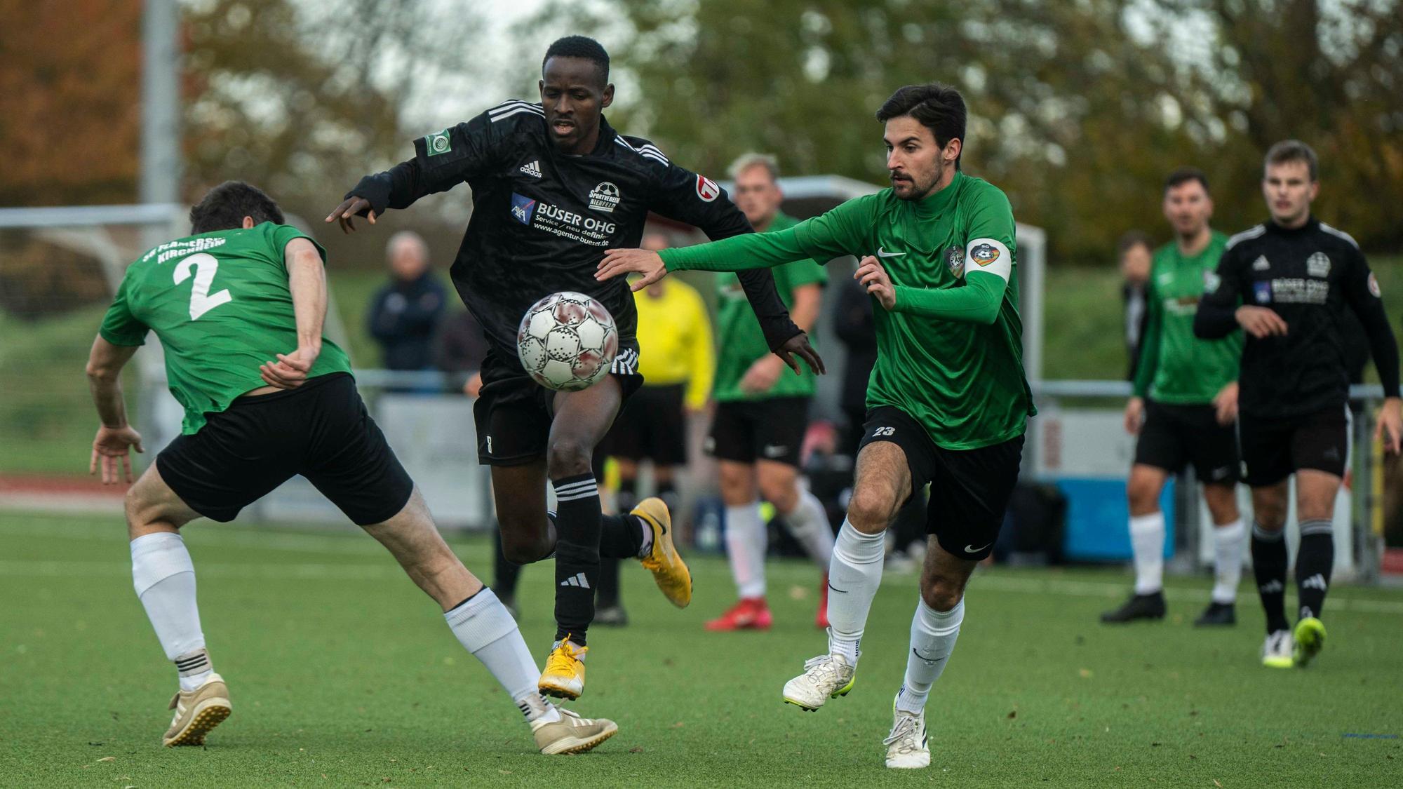 Drei Spieler im Kampf um den Ball. Nierfelds Mory Kaba springt über das ausgestreckte Bein von René Müller, Lukas Mager versucht ihn mit dem Arm auf Abstand zu halten.
