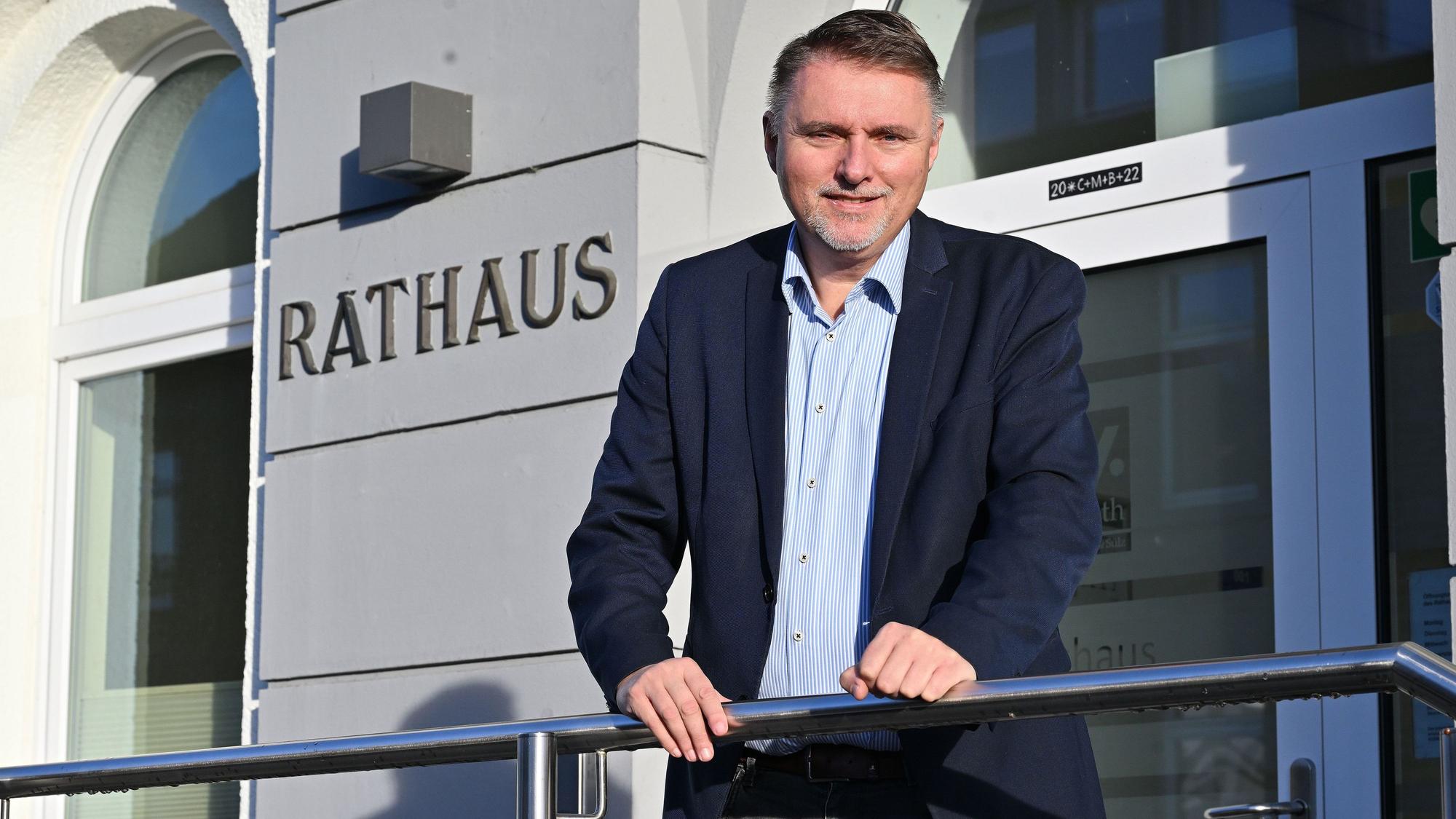 Ein Mann mittleren Alters steht an ein Geländer gelehnt vor einem Rathaus. Er heißt Michael Eyer und ist Bürgermeister von Overath.