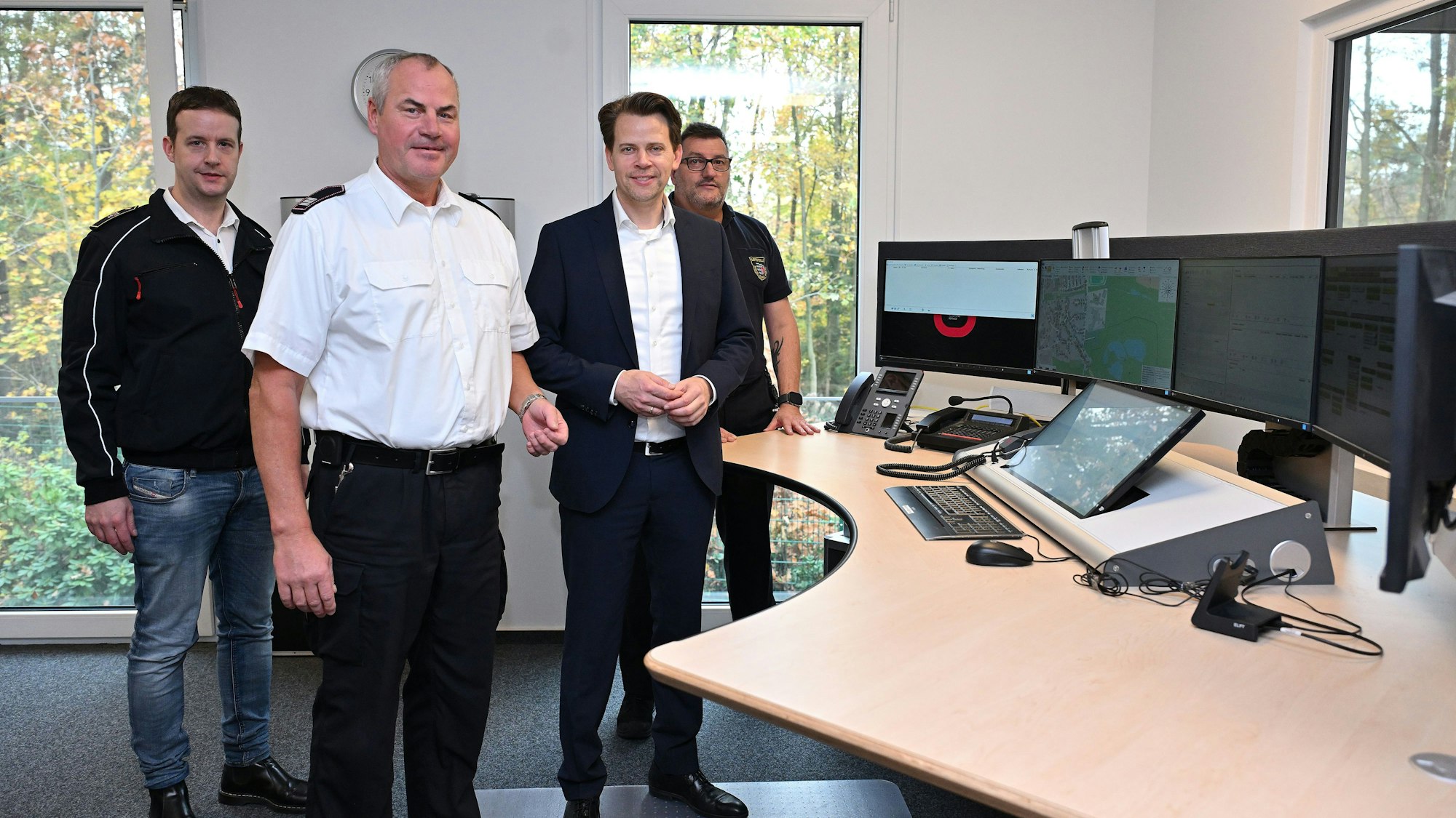 Vier Menschen stehen am Schaltpult in einer Feuerwehr-Leitstelle.