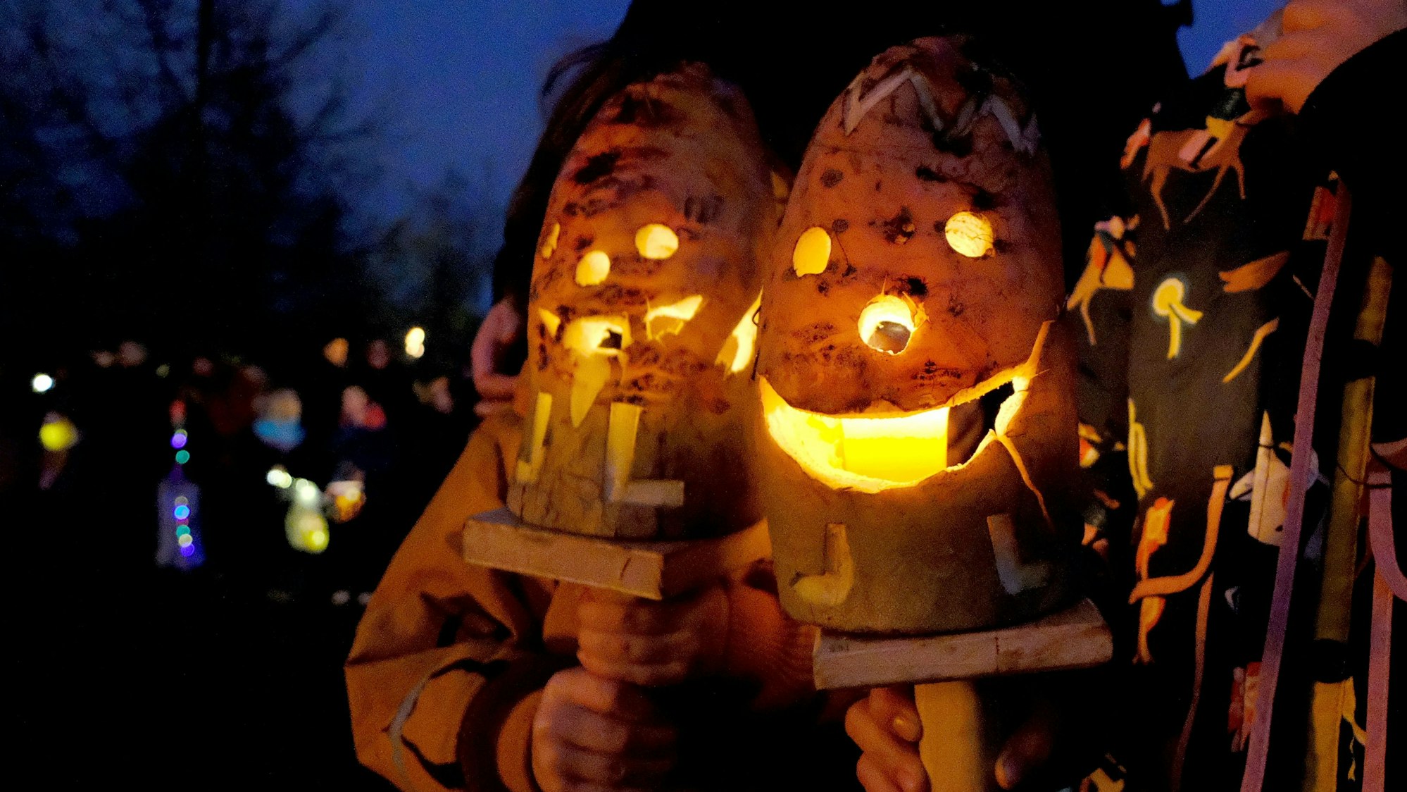 Zwei Kinder halten eine auf einem Holzstab befestigte Rübenlaterne, in die ein Gesicht geschnitzt wurde.