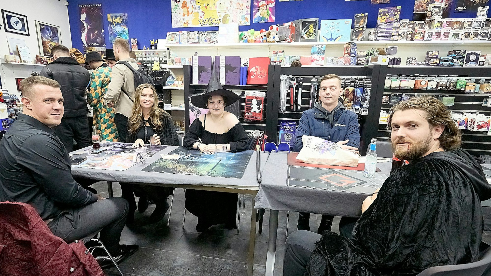 Rund um einen großen Tisch sitzen Personen, zum Teil gruselig kostümiert.