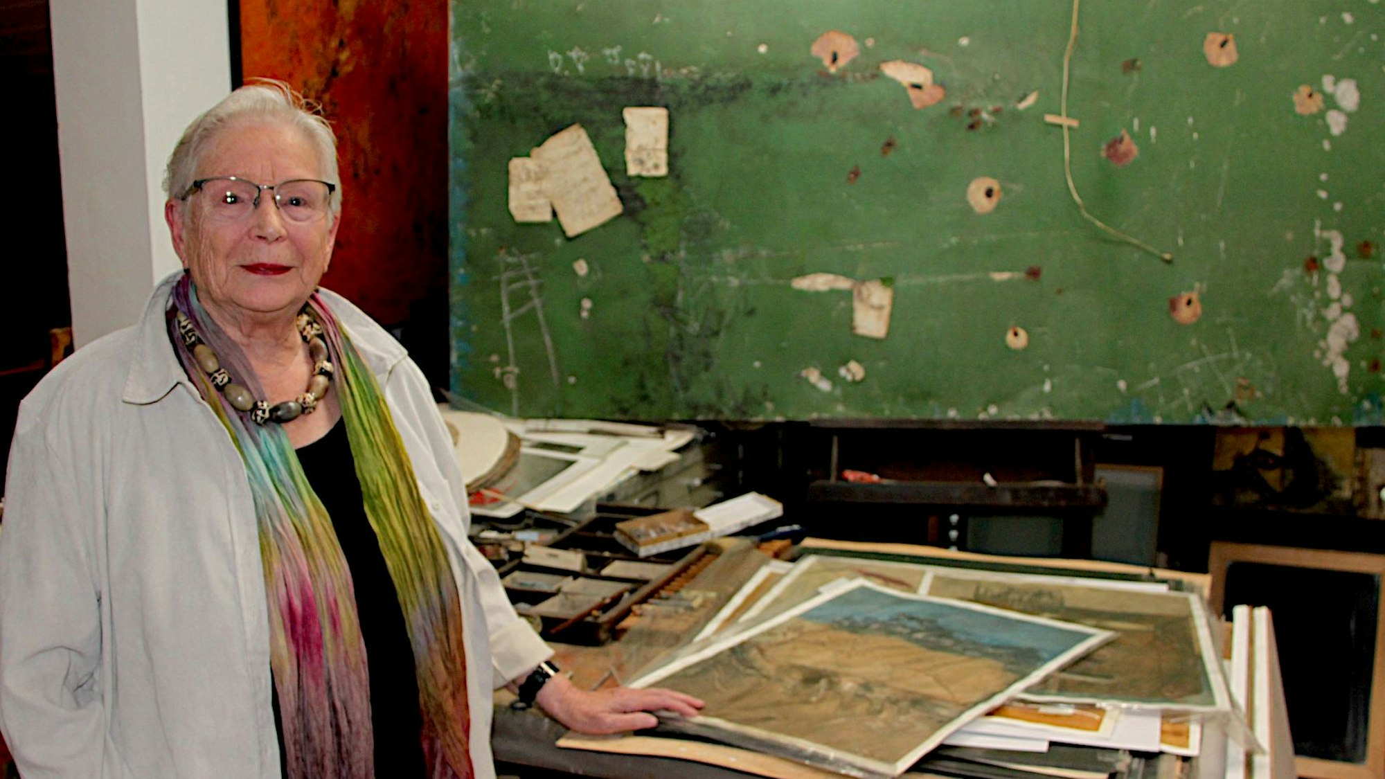 Eva-Maria Hermanns steht im Atelier, vor ihr liegen lose Blätter mit Malereien.