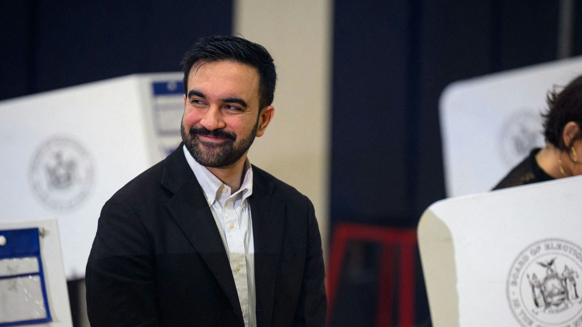 Zohran Mamdani inmitten von Wahlkabinen.