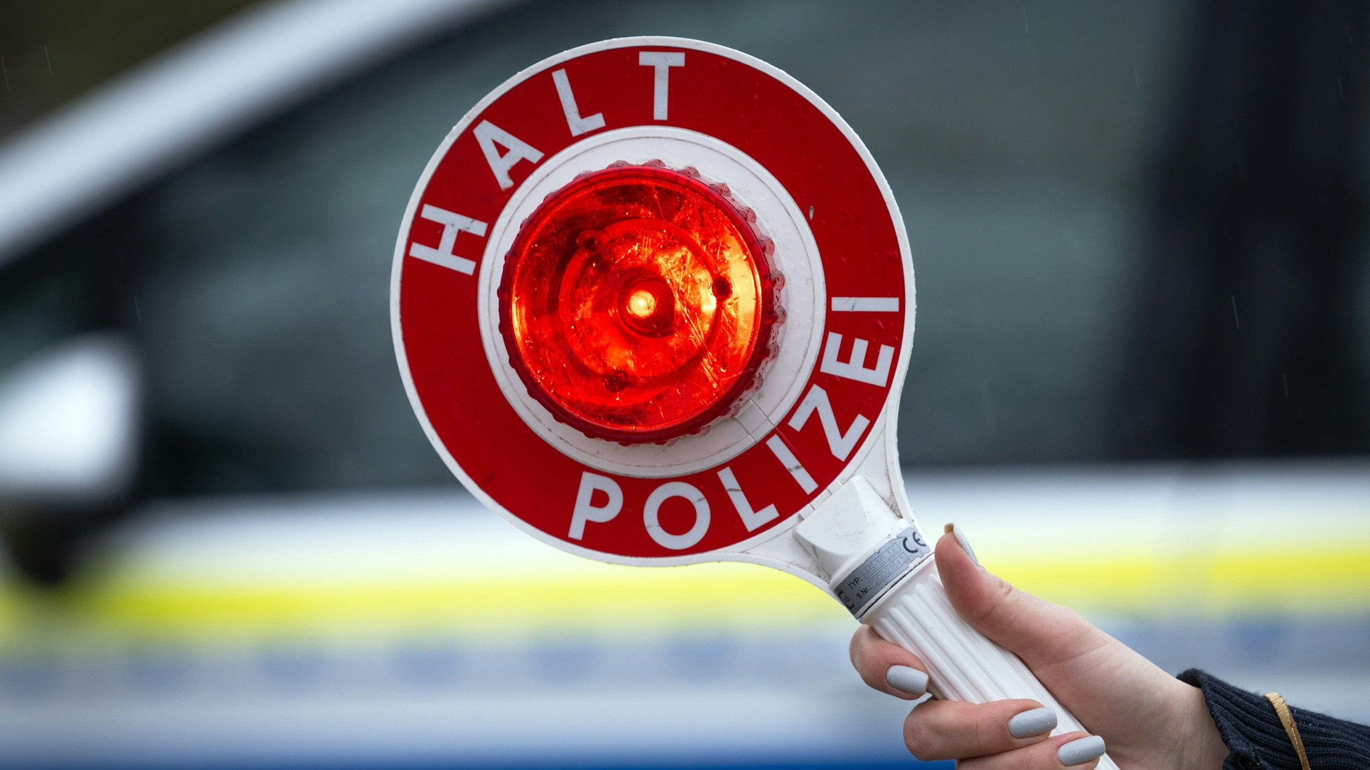Eine Polizistin hält während einer Verkehrskontrolle eine Polizeikelle mit der Aufschrift „Halt Polizei“.
