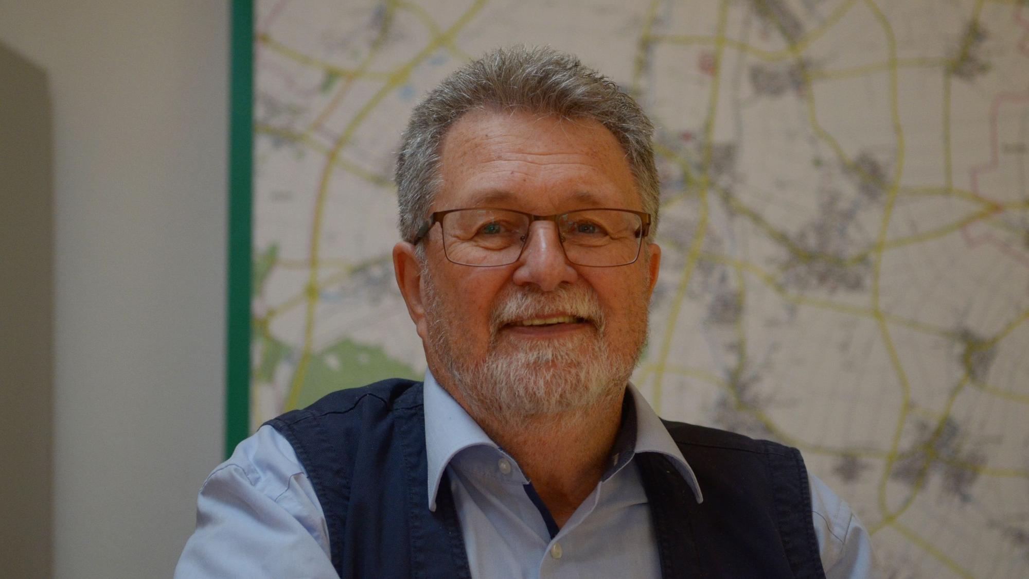 Ein Porträt von Manfred van Bahlen, im Hintergrund verschwommen eine Landkarte.