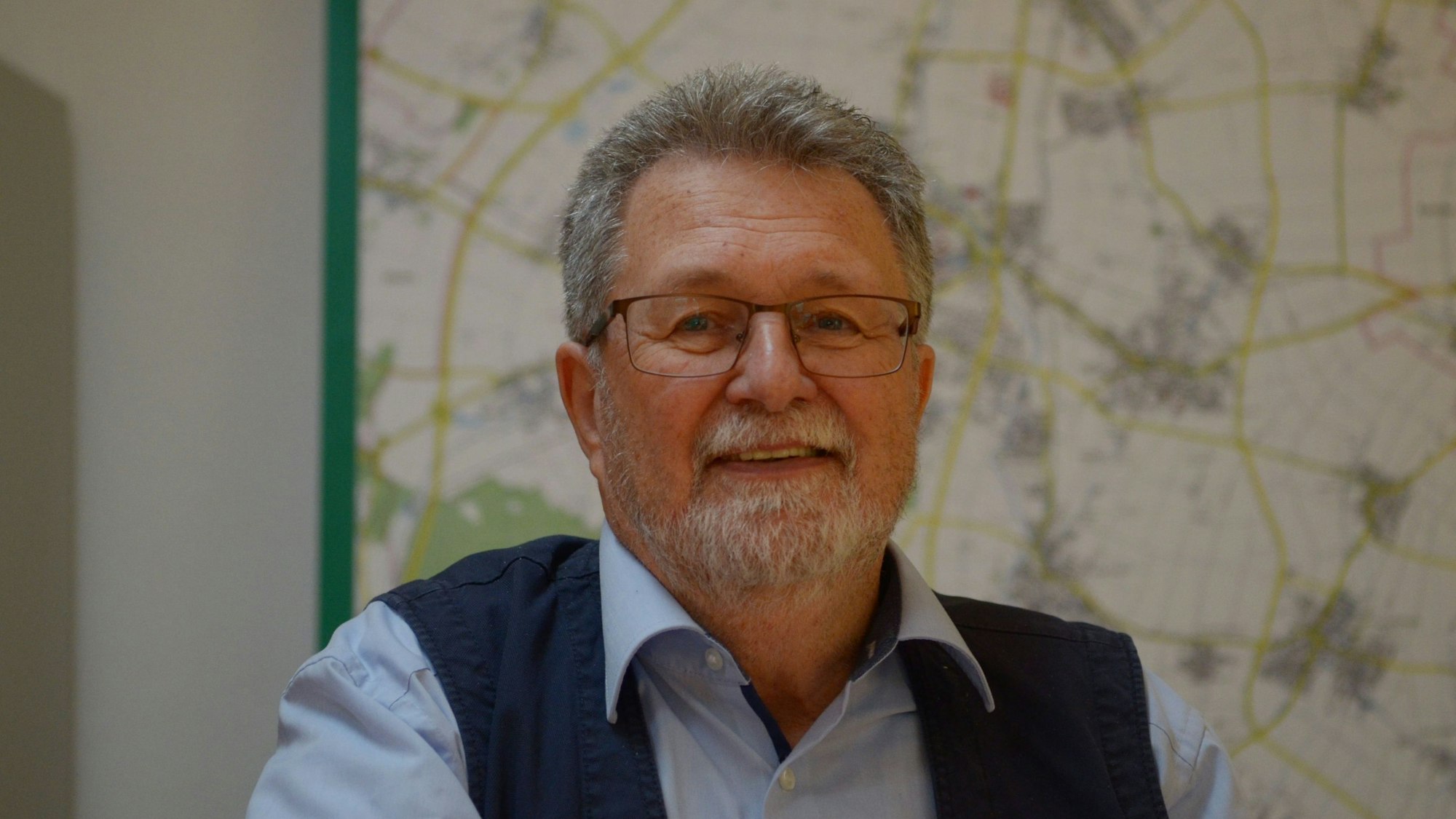 Ein Porträt von Manfred van Bahlen, im Hintergrund verschwommen eine Landkarte.