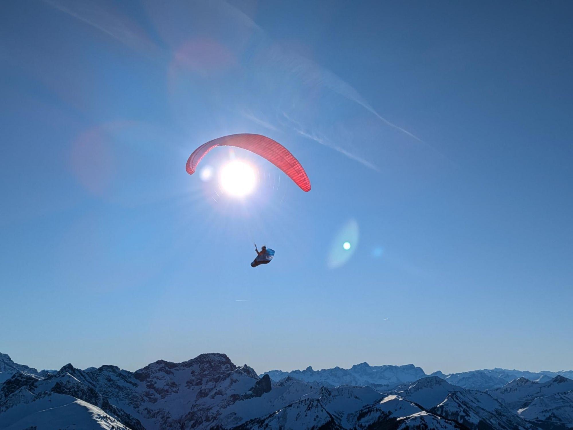 Das Bild zeigt einen Gleitschirmflieger vor einer Sonne.