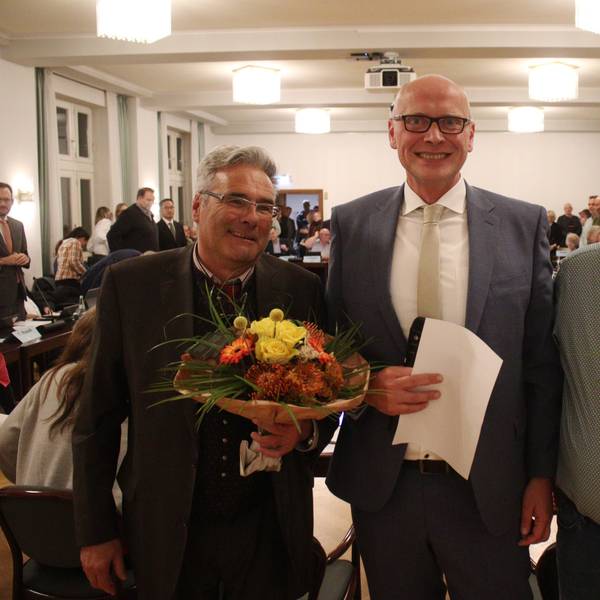 Rechts und links vom Bürgermeister stehen dessen Stellvertreter, die beide Blumen in den Händen halten.