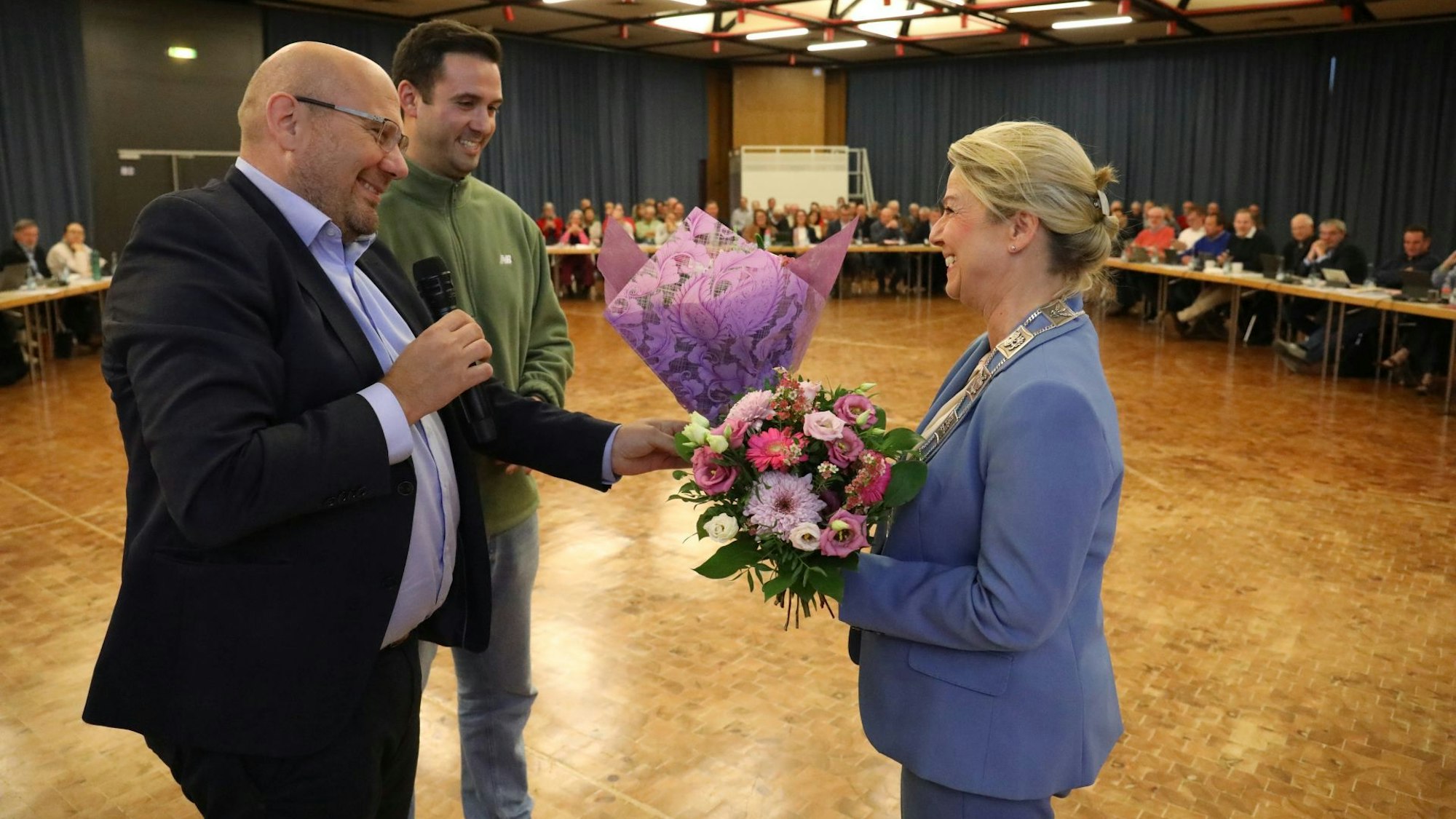 Zwei Männer überreichen einen Blumenstrauß an eine Frau.