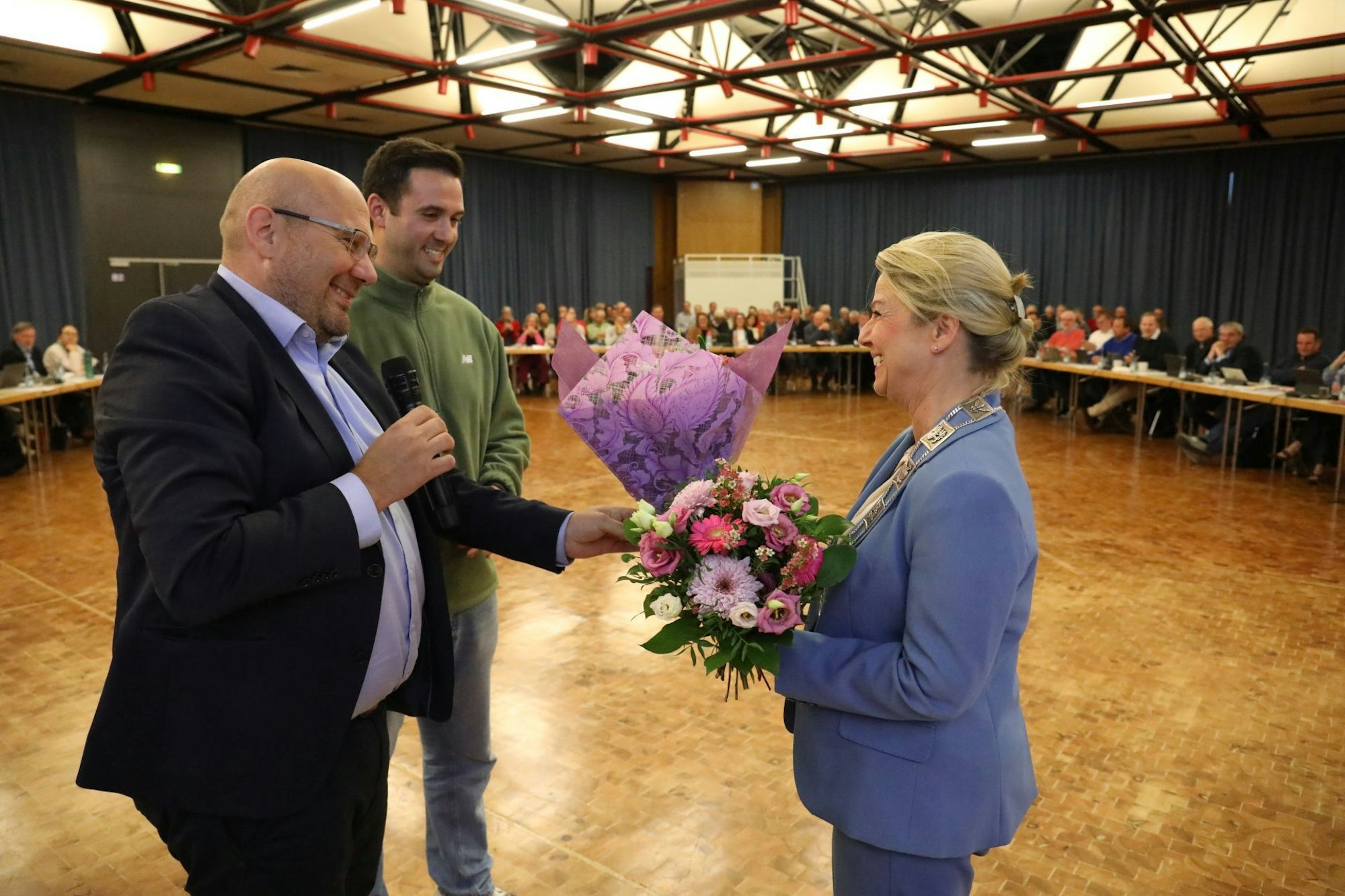 Zwei Männer überreichen einen Blumenstrauß an eine Frau.