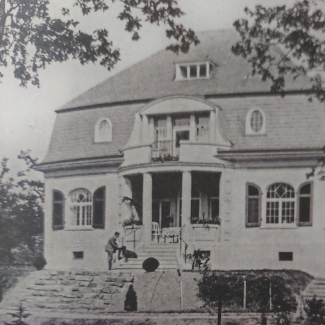 Eine Villa mit Walmdach und einem herrschaftlichen Treppenaufgang mit Säuleneingang.