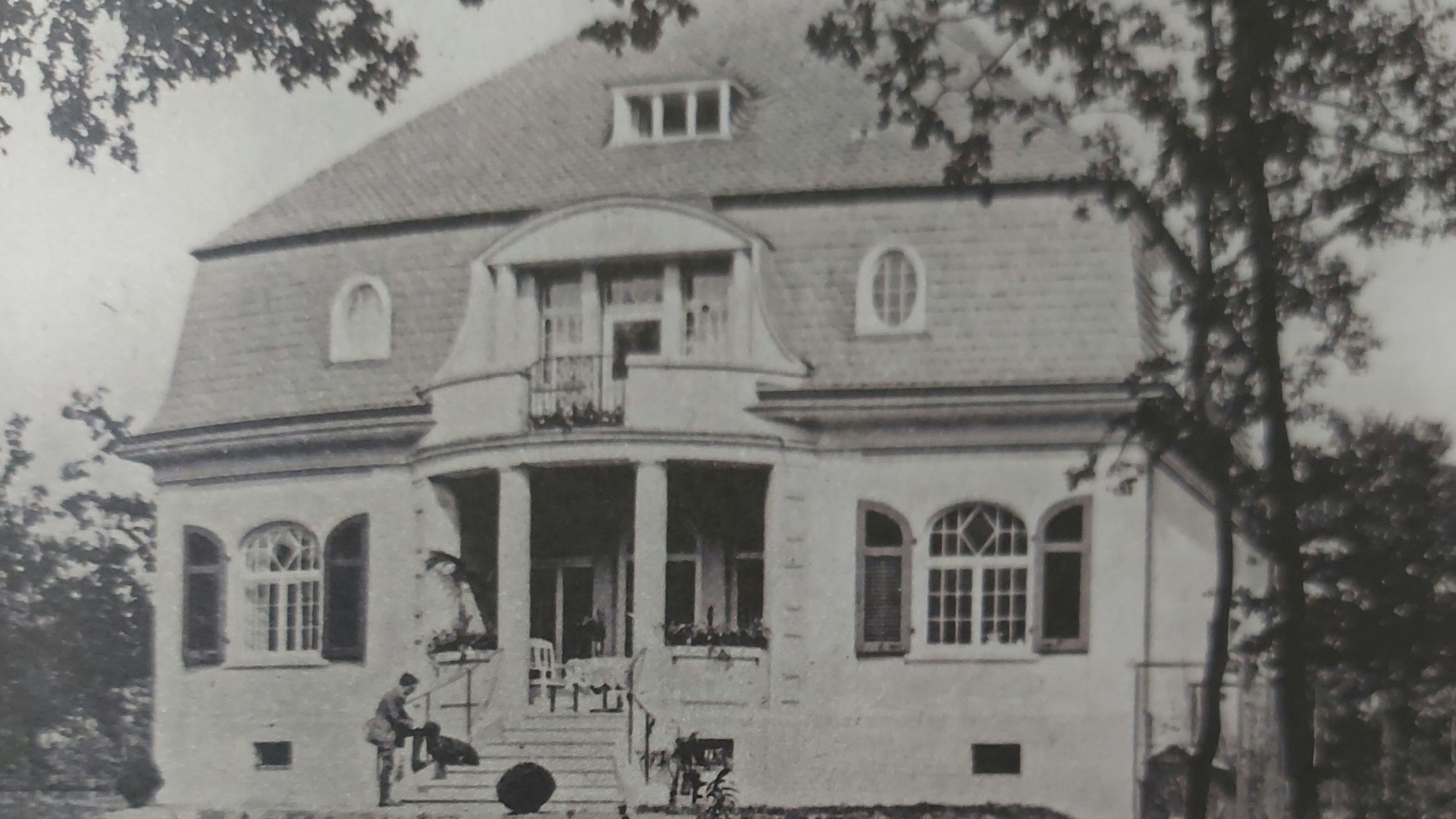 Eine Villa mit Walmdach und einem herrschaftlichen Treppenaufgang mit Säuleneingang.