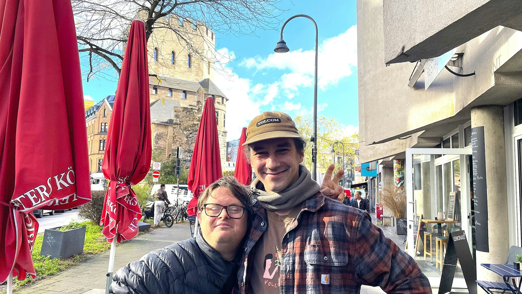Ein kleiner Mann mit Brille wird von einem großen mit Kappe in den Arm genommen.