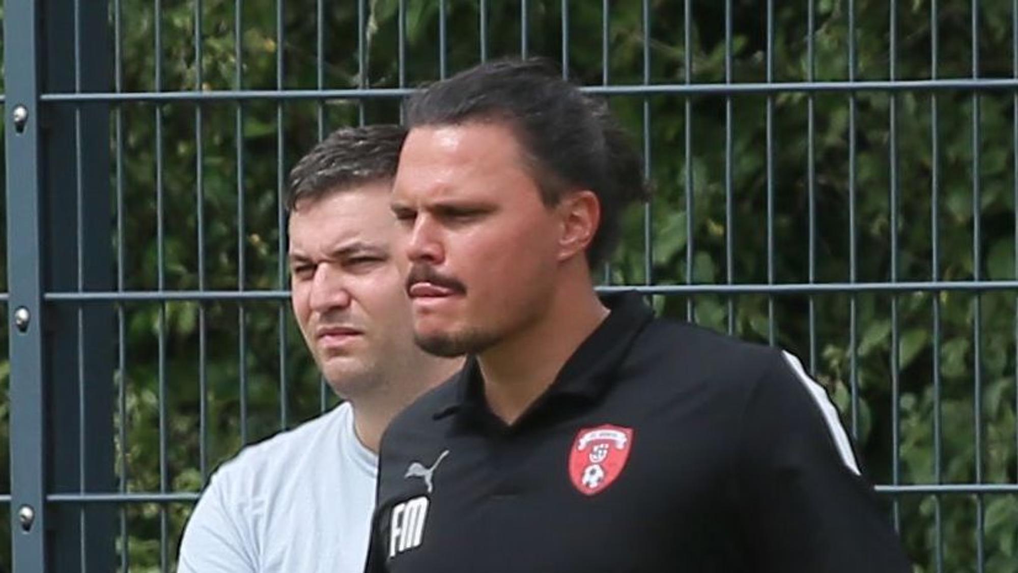 Das Bild zeigt Fabian Montabell in einem schwarzen T-Shirt, der das Spiel seiner Elf beobachtet.