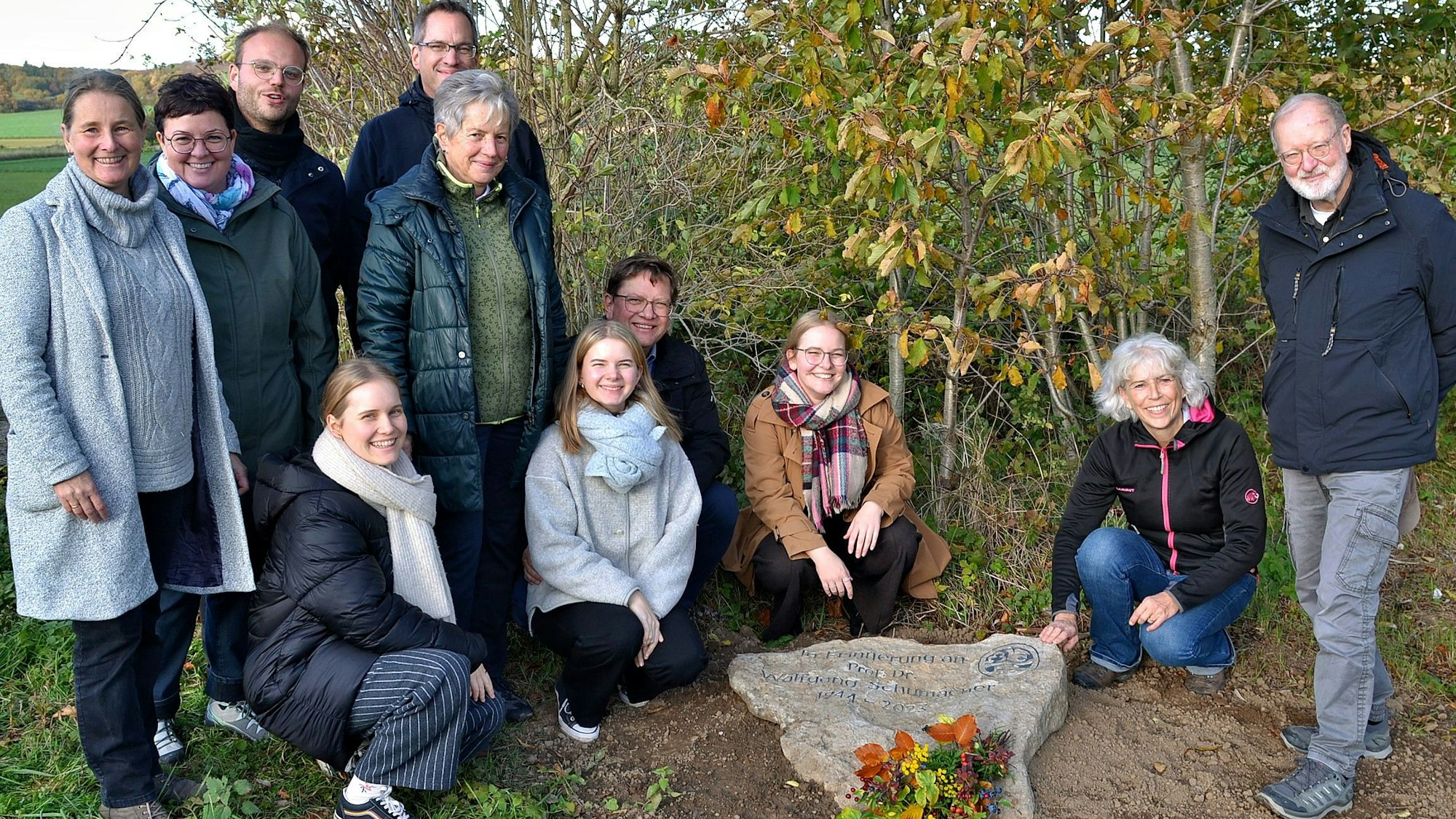 Um den frisch verlegten Gedenkstein stehen und knien Angehörige und Wegbegleiter Schumachers.