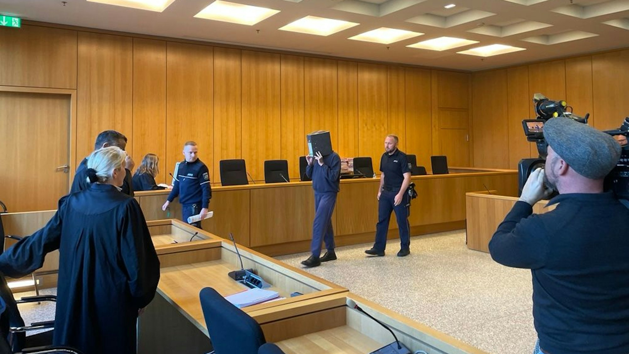 Der ehemalige Krankenpfleger, der wegen zehnfachen Mordes und 27-fachen Mordversuchs zu einer lebenslangen Freiheitsstrafe verurteilt wurde, verbirgt sein Gesicht hinter einem Aktenordner, als er in den Verhandlungssaal am Landgericht Aachen geführt wird. Foto: Detlef Schmalenberg